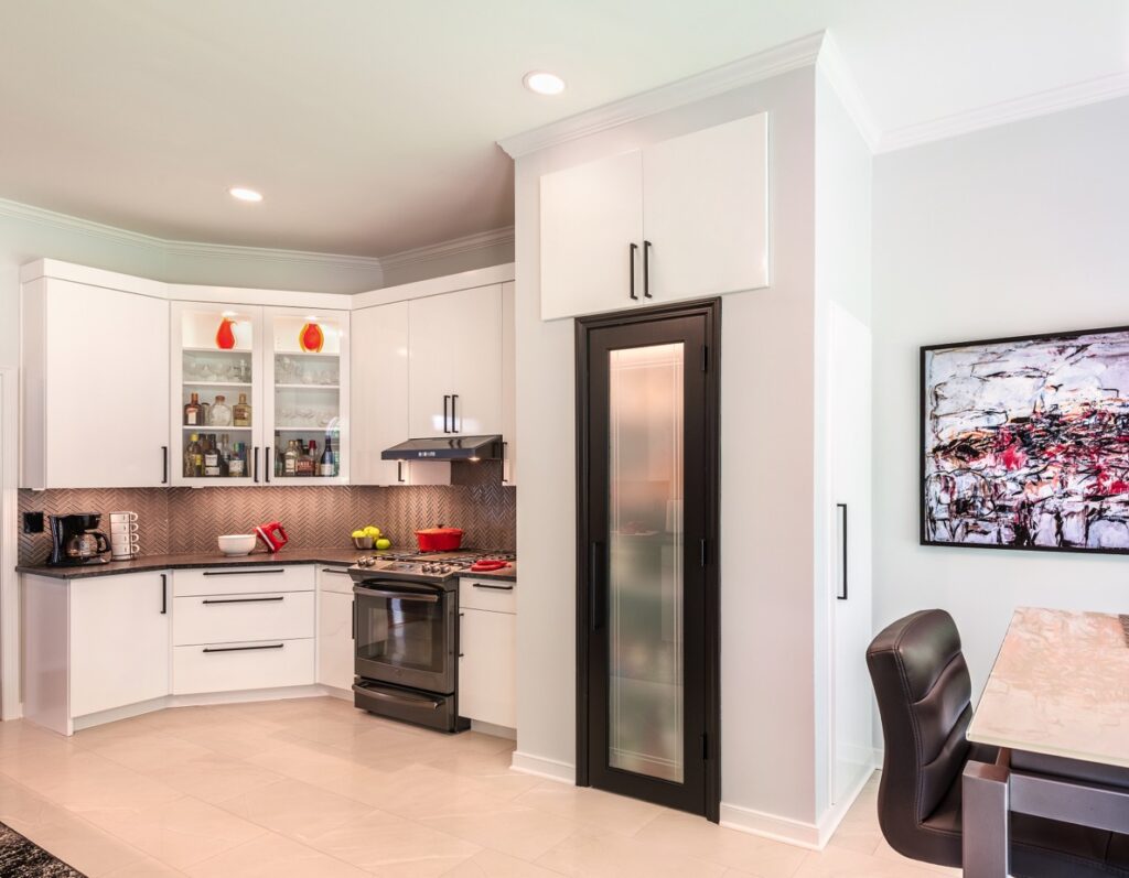 High-gloss white cabinetry extending to a 9.5-foot ceiling in a contemporary kitchen remodel featuring a custom black-framed frosted glass pantry door.