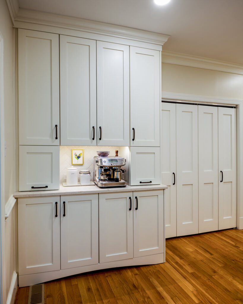 Built-in white shaker coffee bar and pantry station with integrated appliance garage doors, an espresso machine, and adjacent white laundry closet bi-fold doors.