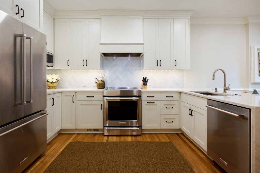 Straight-on view of the kitchen cooking zone featuring a stainless steel range, custom white cabinetry hood, herringbone tile backsplash, and counter-depth refrigerator.